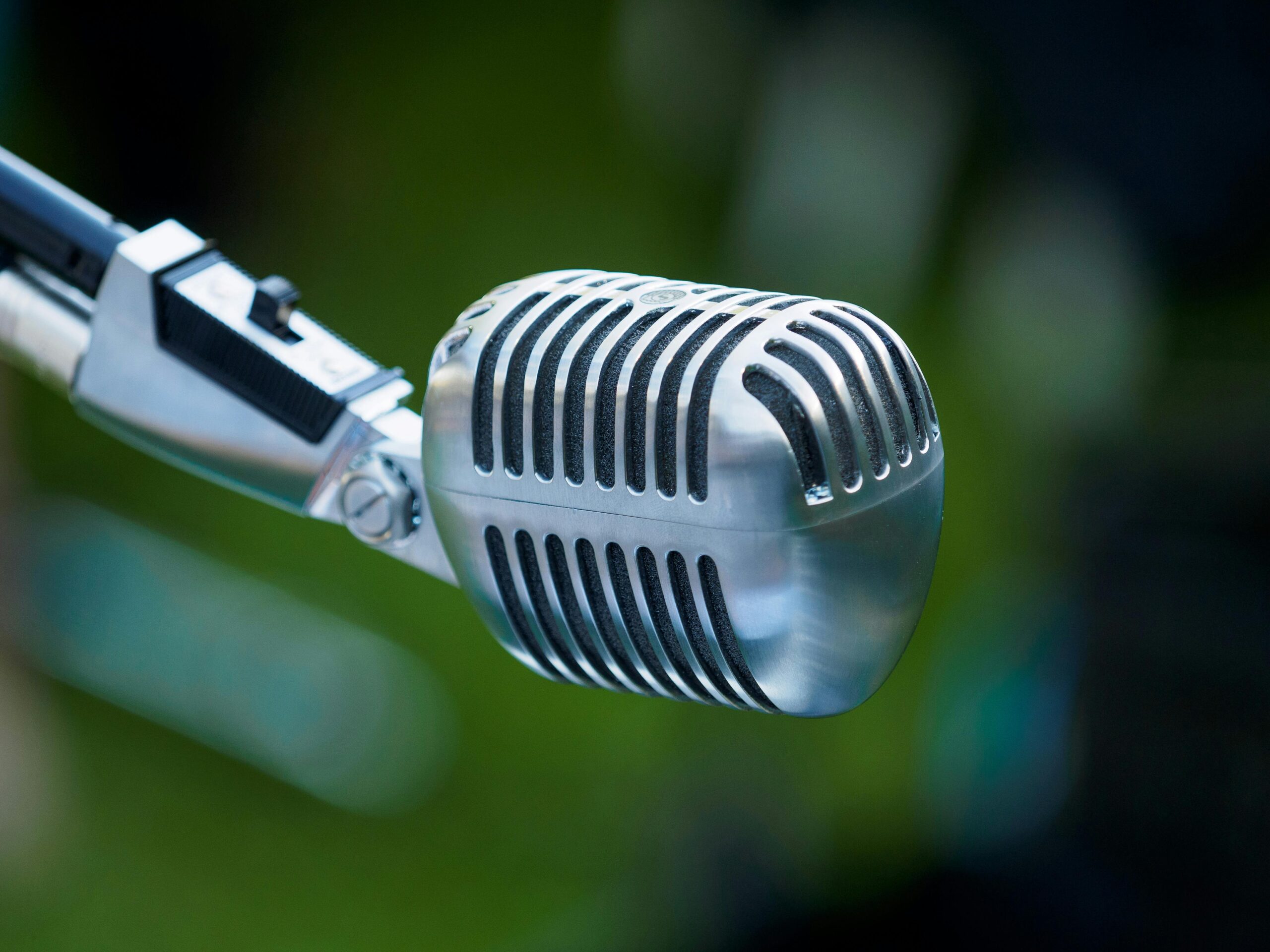 Classic chrome vintage microphone with defocused green outdoor background.