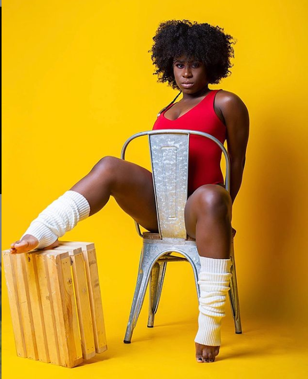 African American presenting woman with red top seated in chair and leg warmers in fit