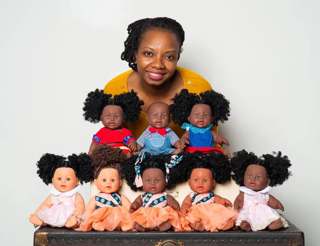 woman of african decsent standing over a pyramid of 8 black baby dolls. 