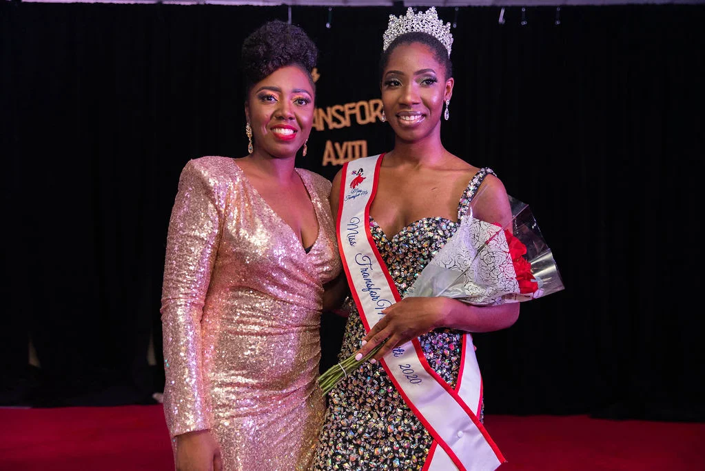 Two women of african decent stand side by side in shiny gowns. TO the right the woman has a crown and sash.