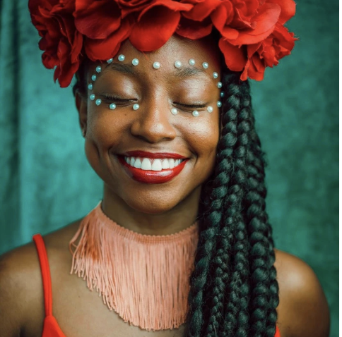 woman with african decent with braids and. red floral crown.